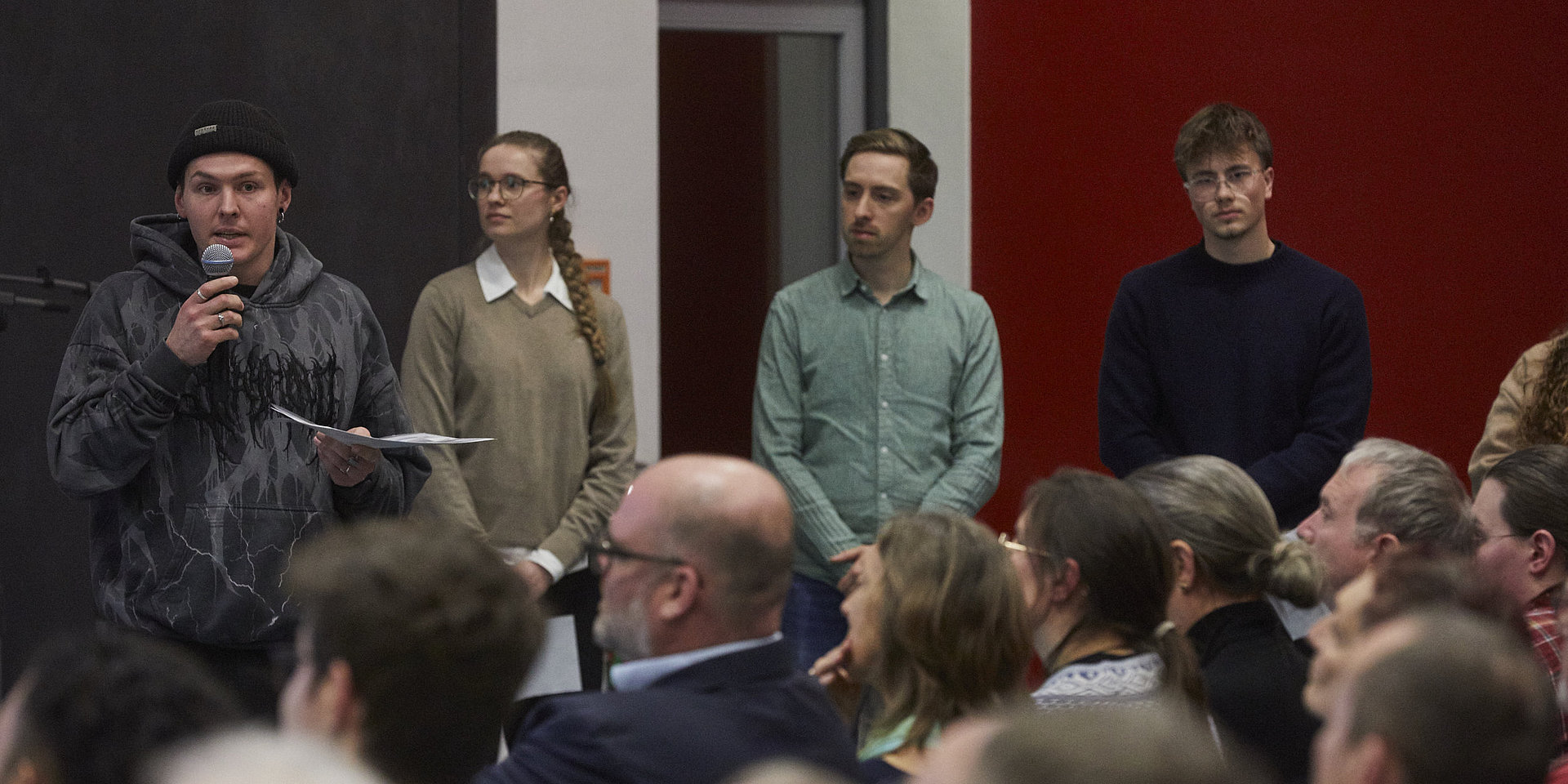 Vier Studenten stehen auf einer Bühne vor einem großen Publikum.
