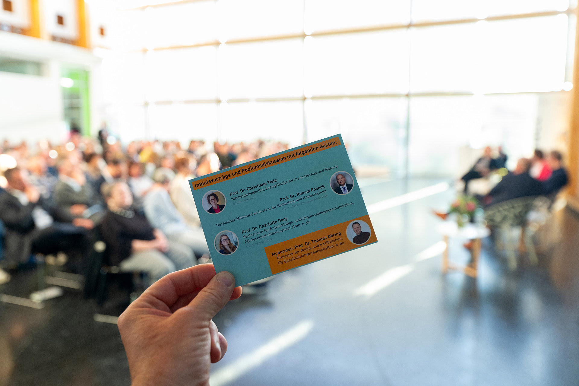 The invitation card for the dialogue forum in the foreground, with the auditorium blurred in the background.
