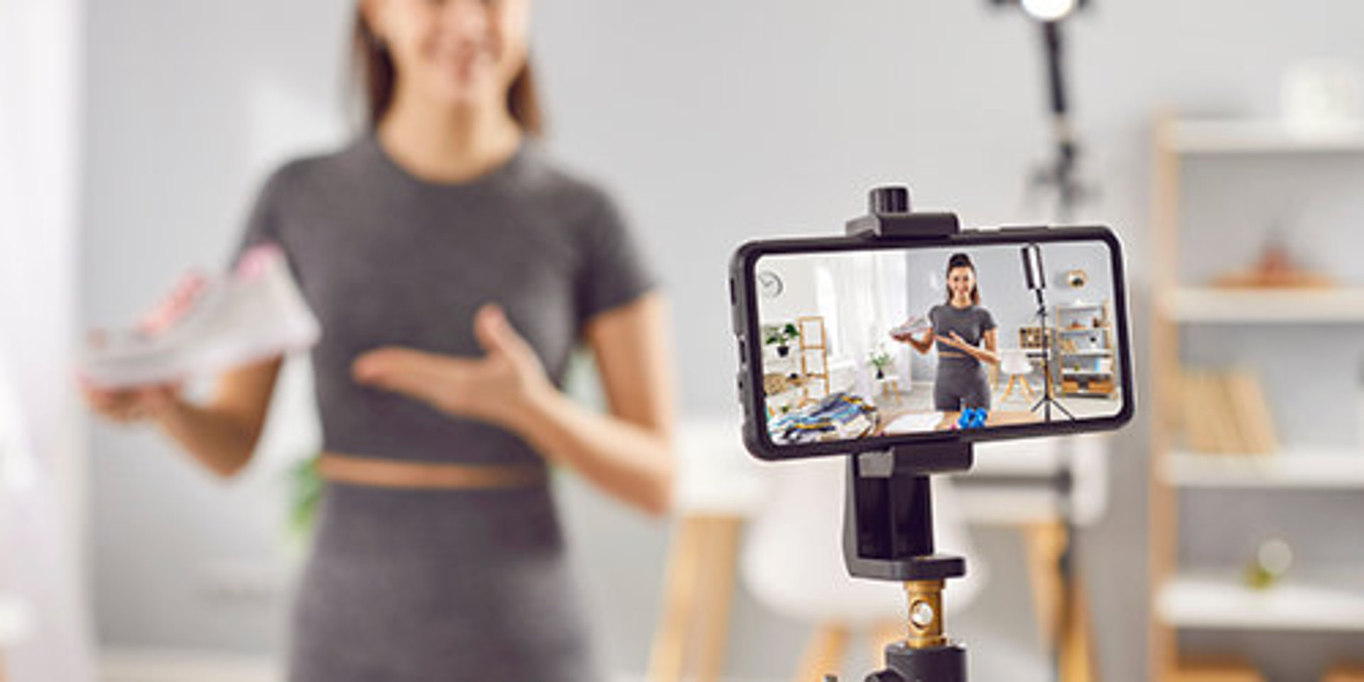 Influencerin verschwommen im Hintergrund mit Video-Handy im Vordergrund.