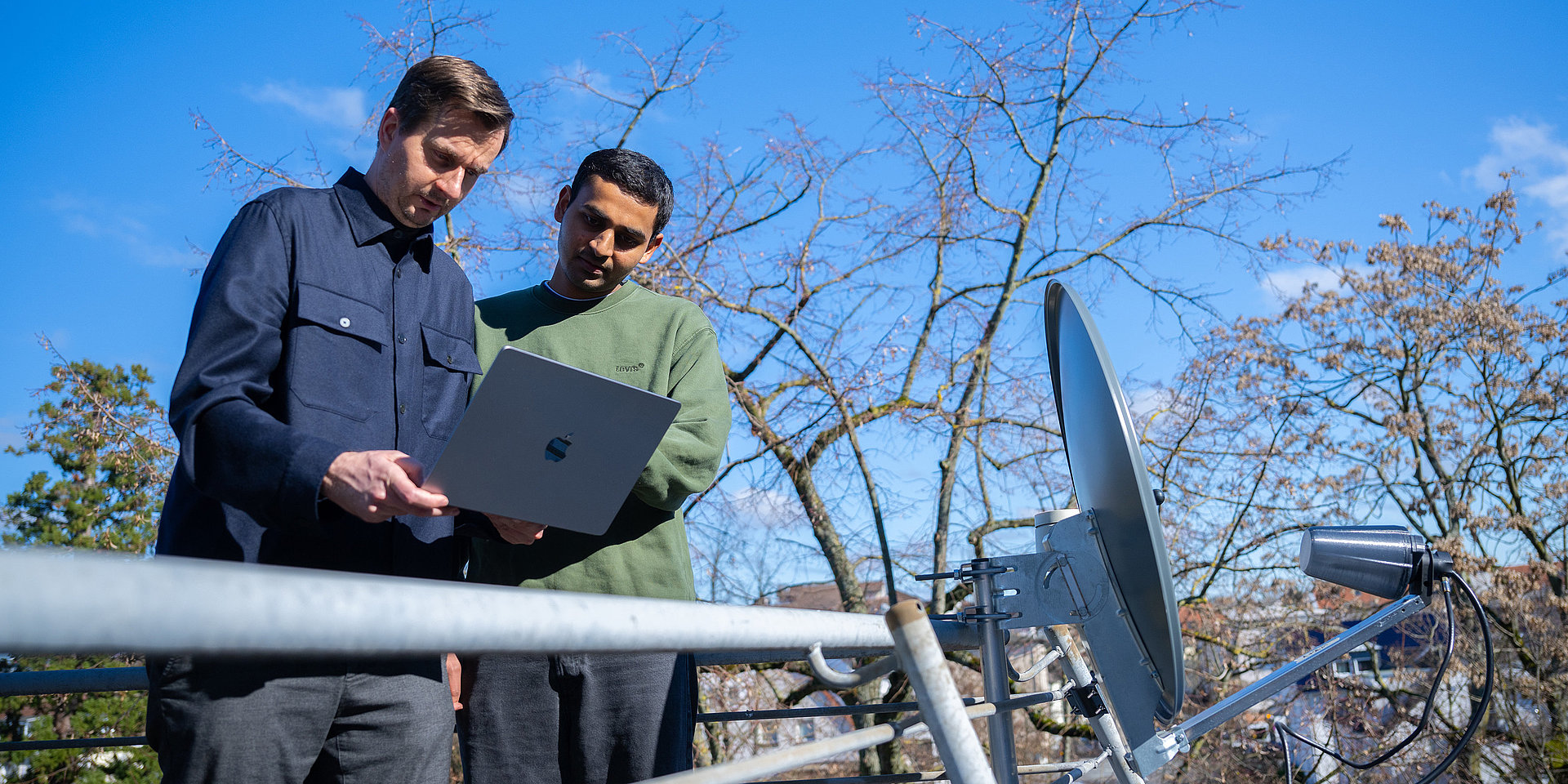 Professor Valentin und Student Vedant Vedant stehen neben der Satellitenschüssel auf einem Balkon des Fachbereichs Informatik