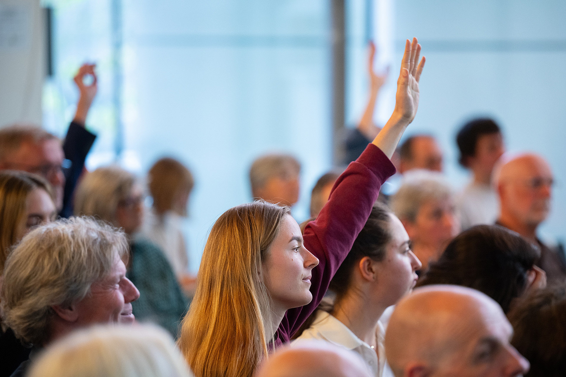 Several guests raise their hands to ask a question.