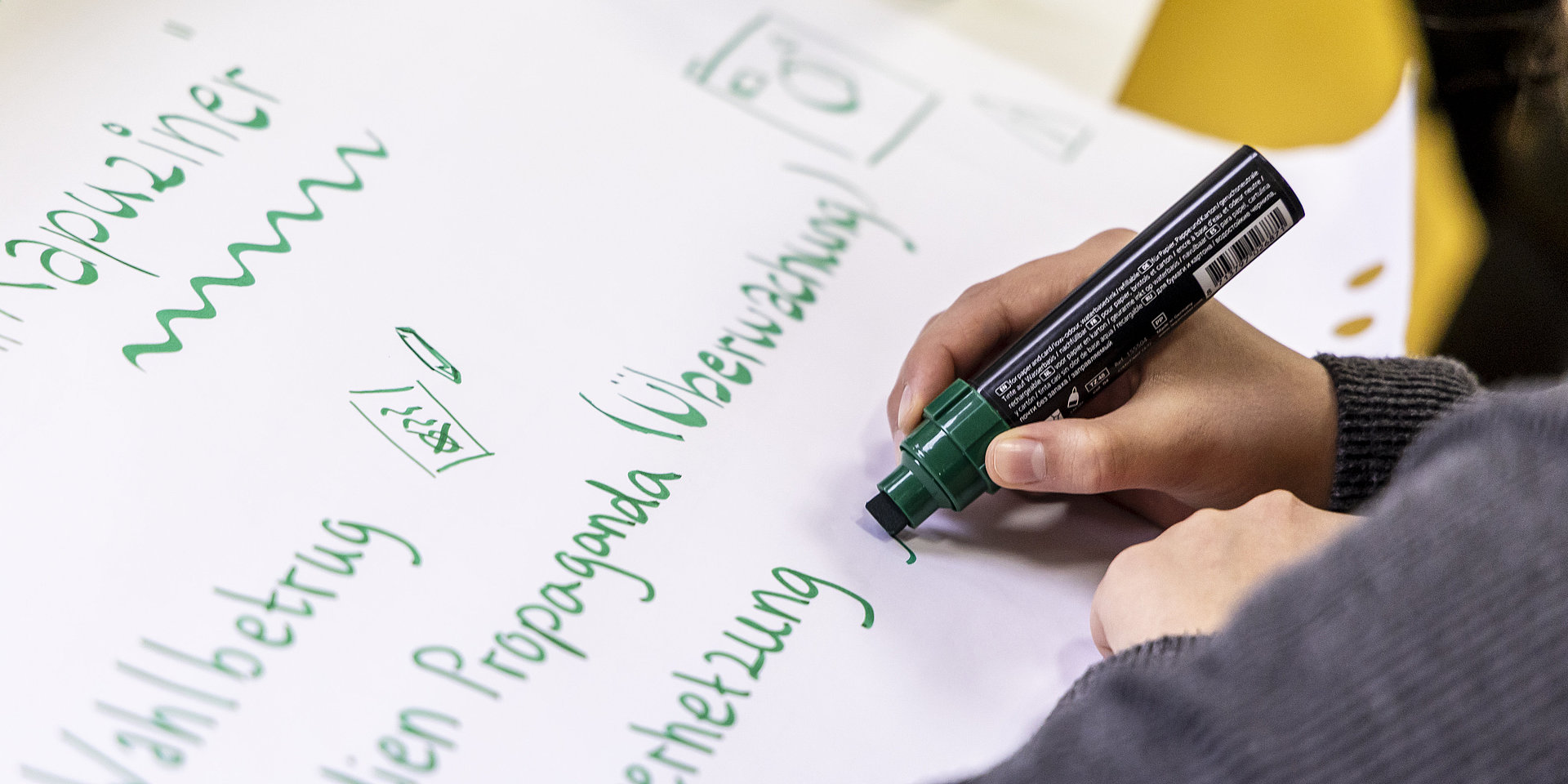 A view over the shoulder of a participant holding a pen and writing on a sheet of paper.