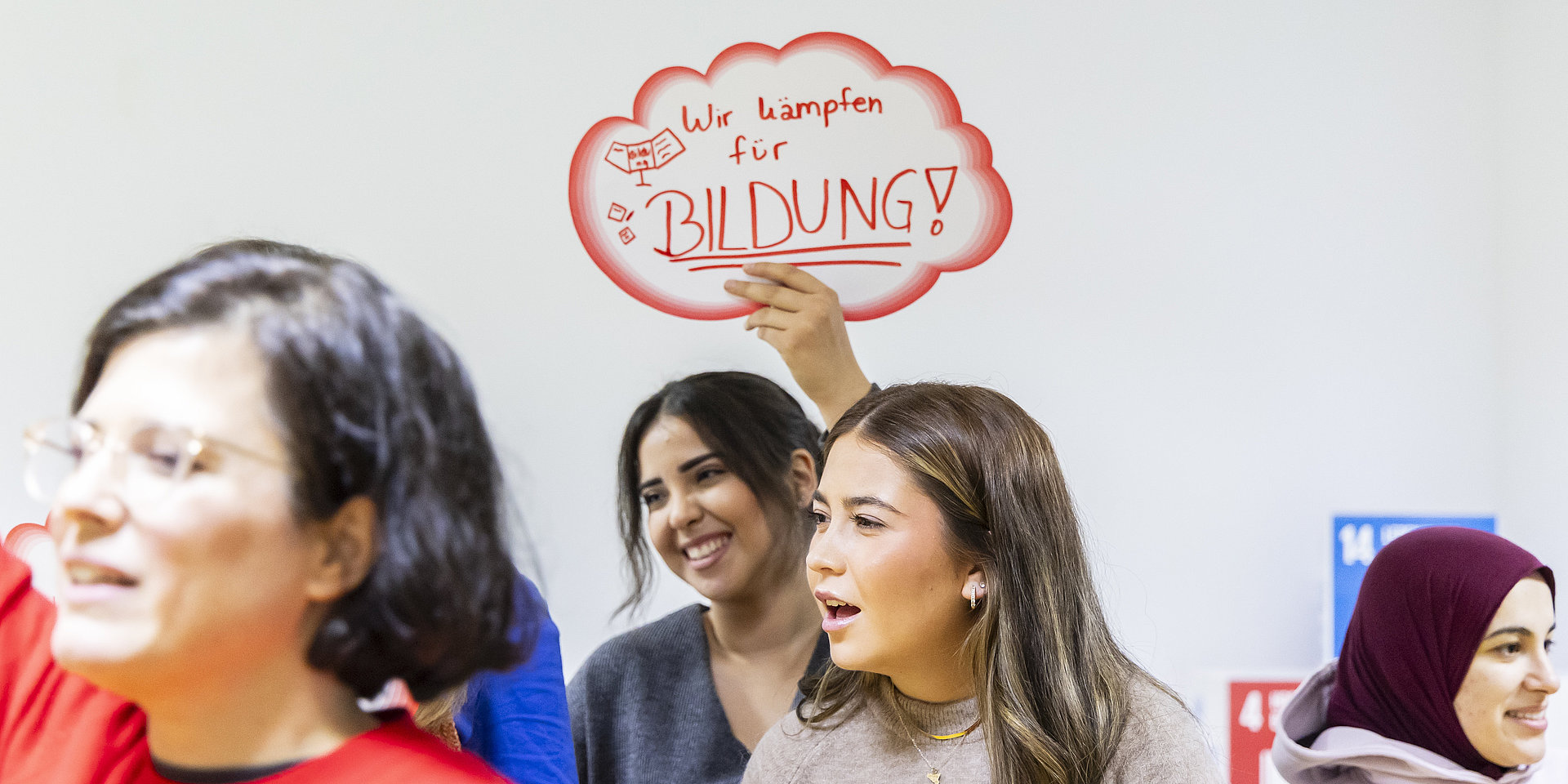 Zwei junge Frauen halten ein rot umrandetes Schild mit einem Slogan in die Höhe.