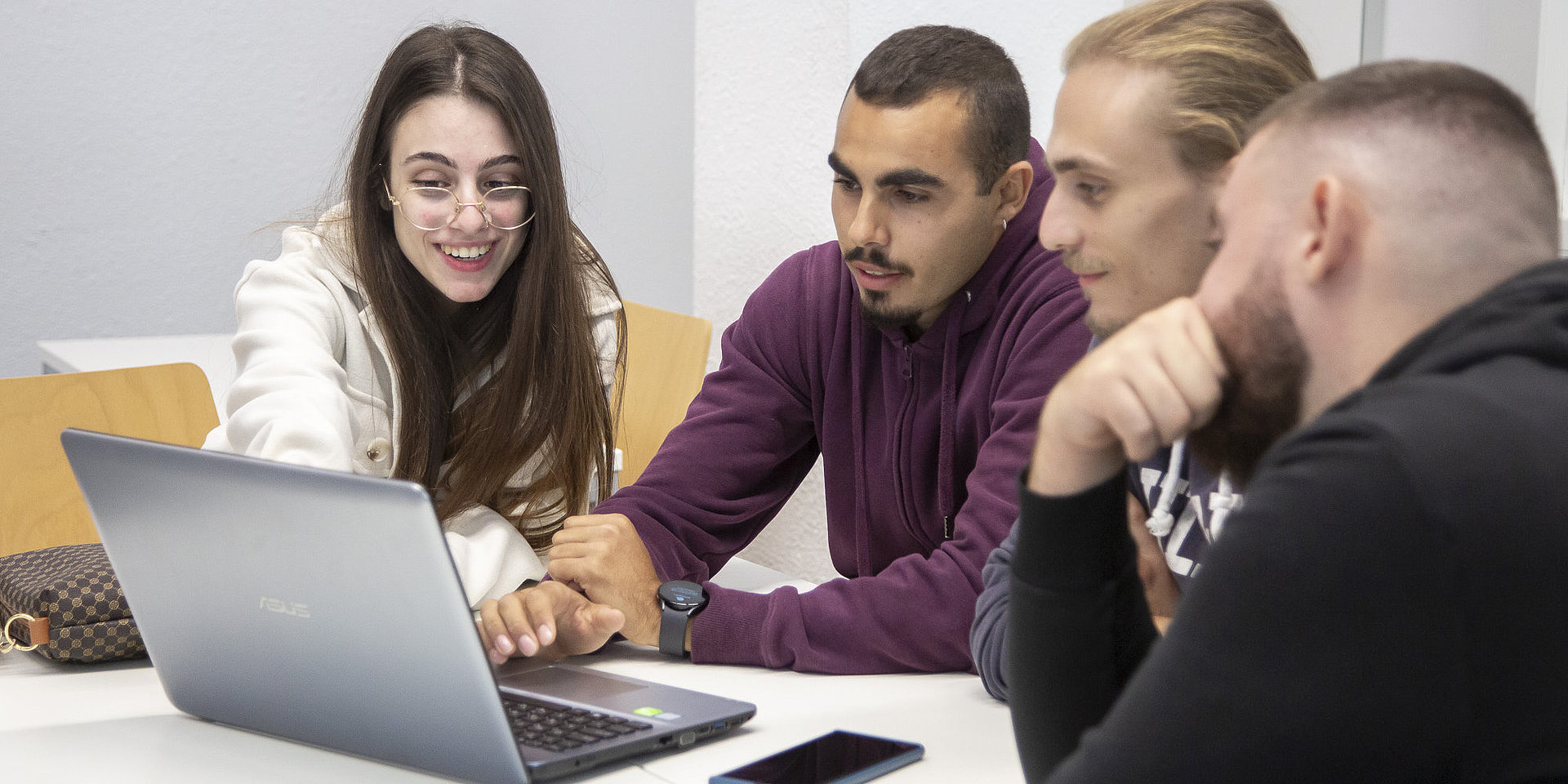 Vier Studenten schauen auf einen Laptop.