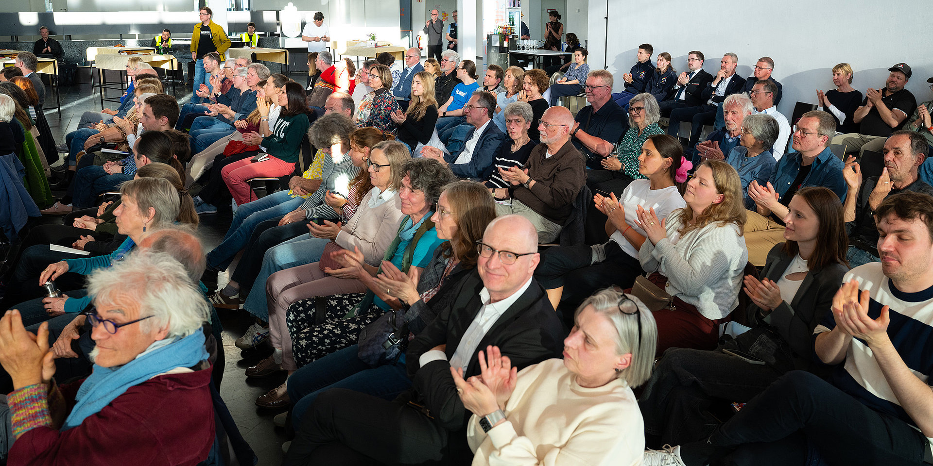 Die Gäste im Foyer applaudieren den Vortragenden.