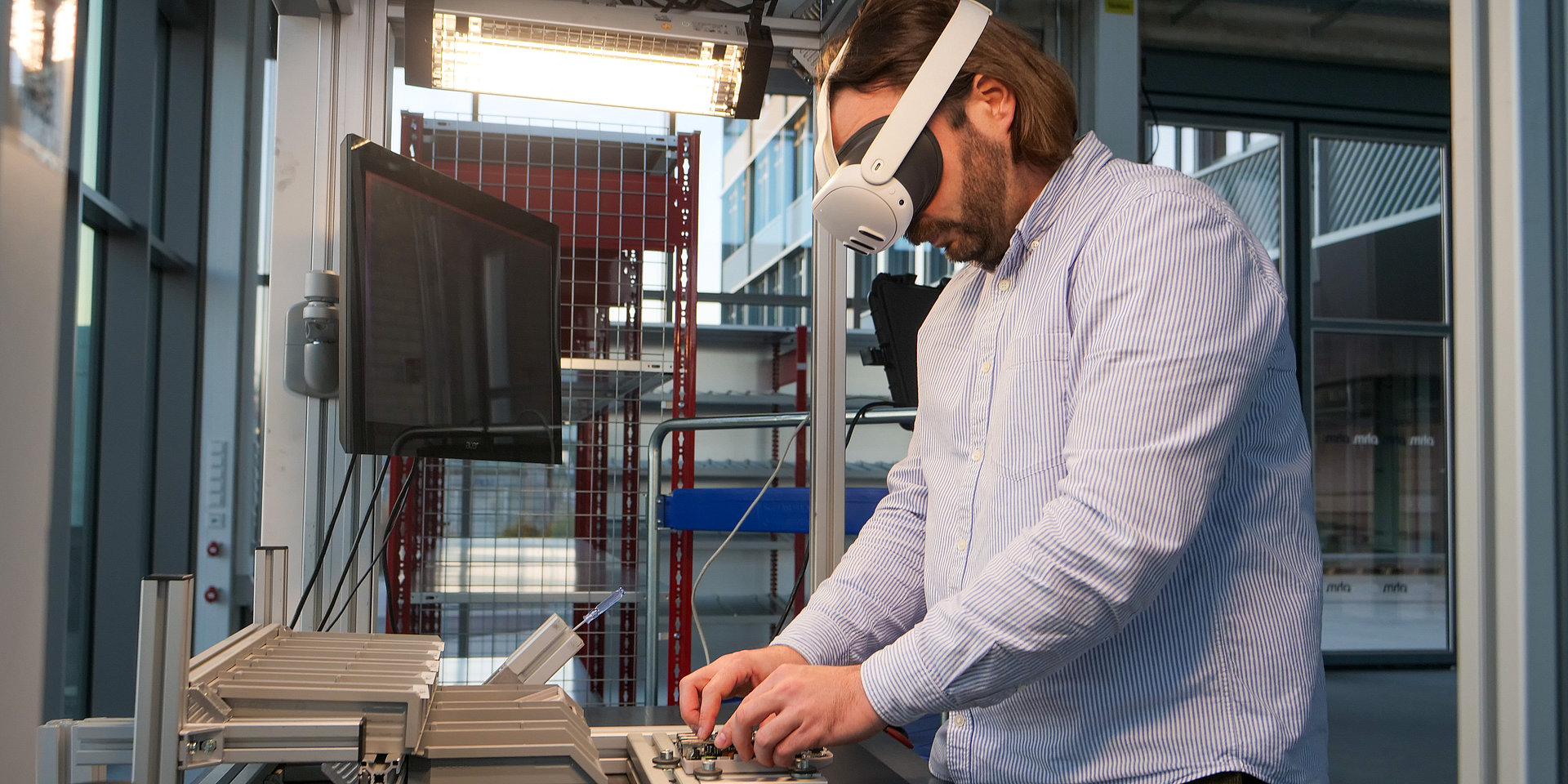 Fabian Sturm is pictured wearing VR goggles and assembling a component on a workbench.