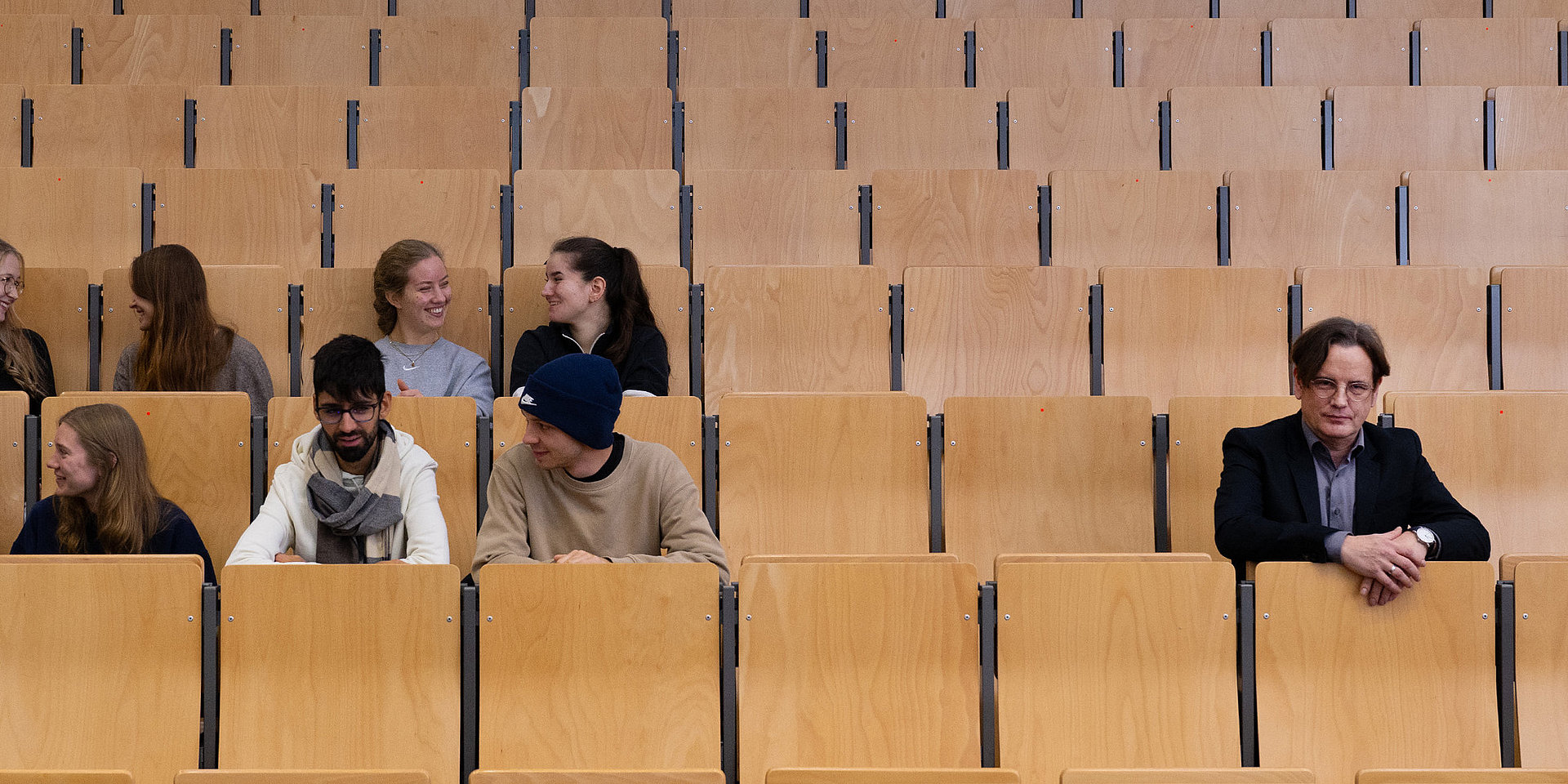 Studierende sitzen als Gruppe in einem Hörsaal, rechts davon Professor Mario Rund