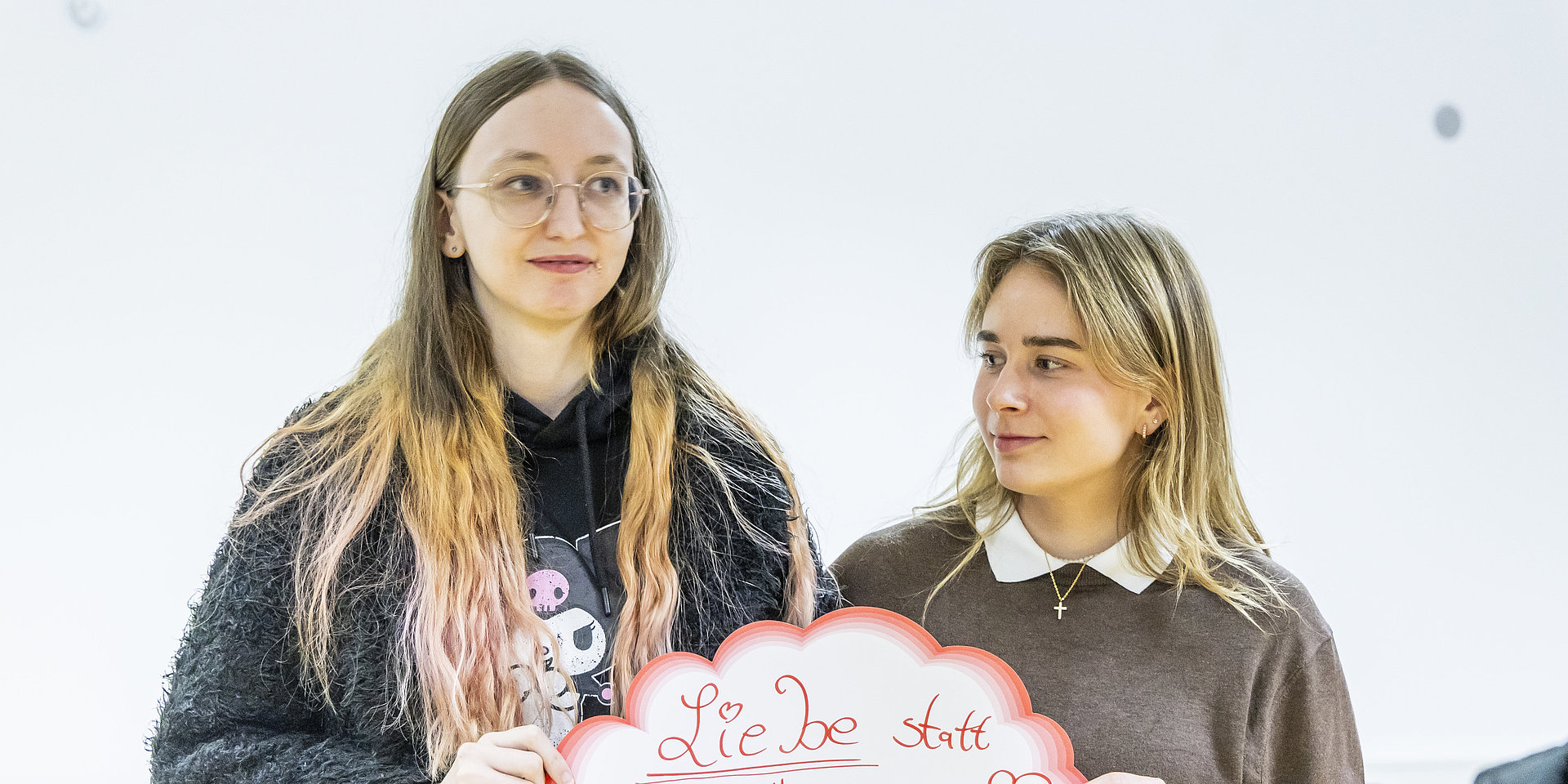 Zwei Studentinnen präsentieren ein rot umrandetes Schild mit dem Slogan "Liebe statt Hass".