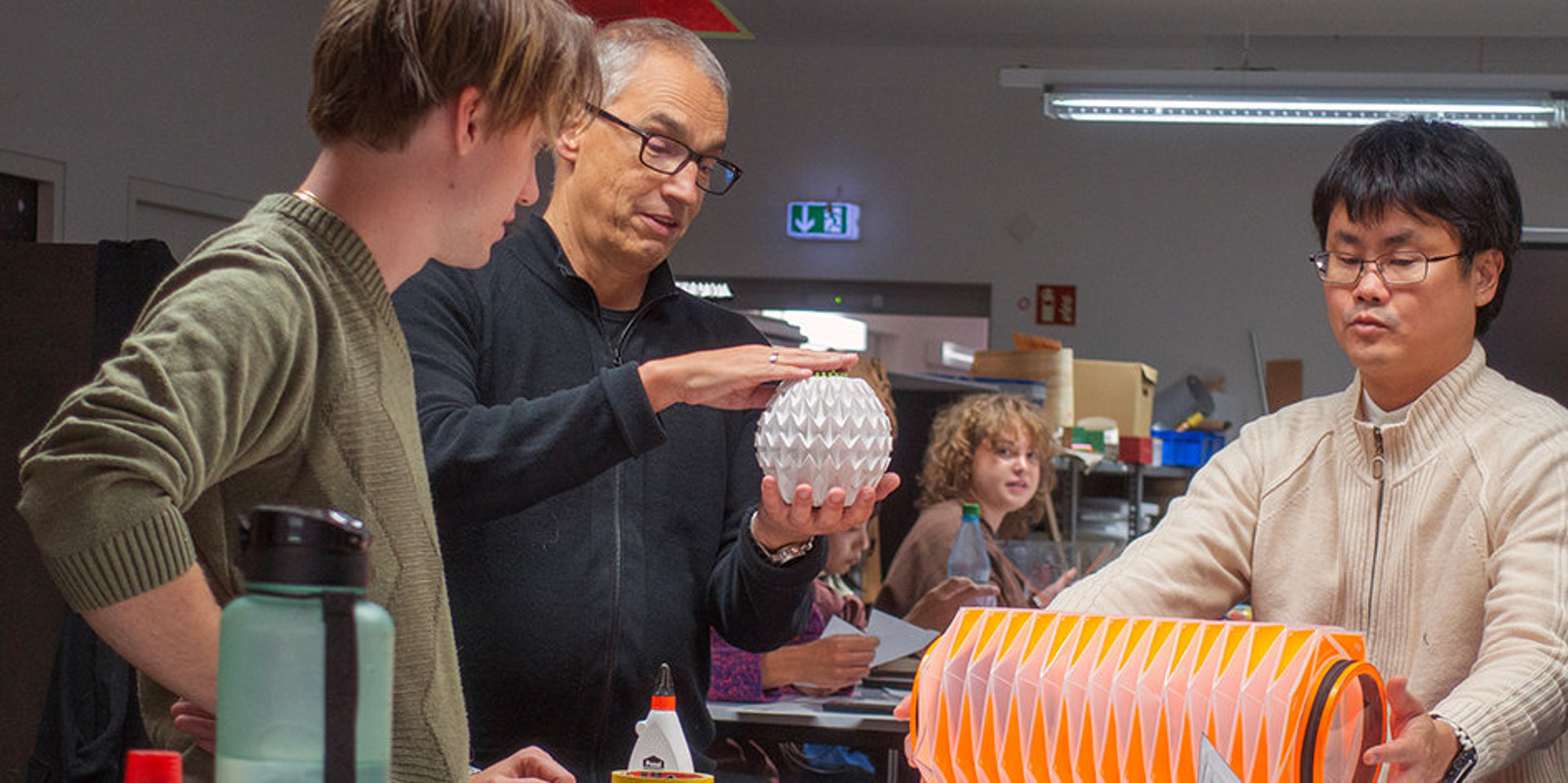 Ein Professor erklärt zwei Studenten das Origami.