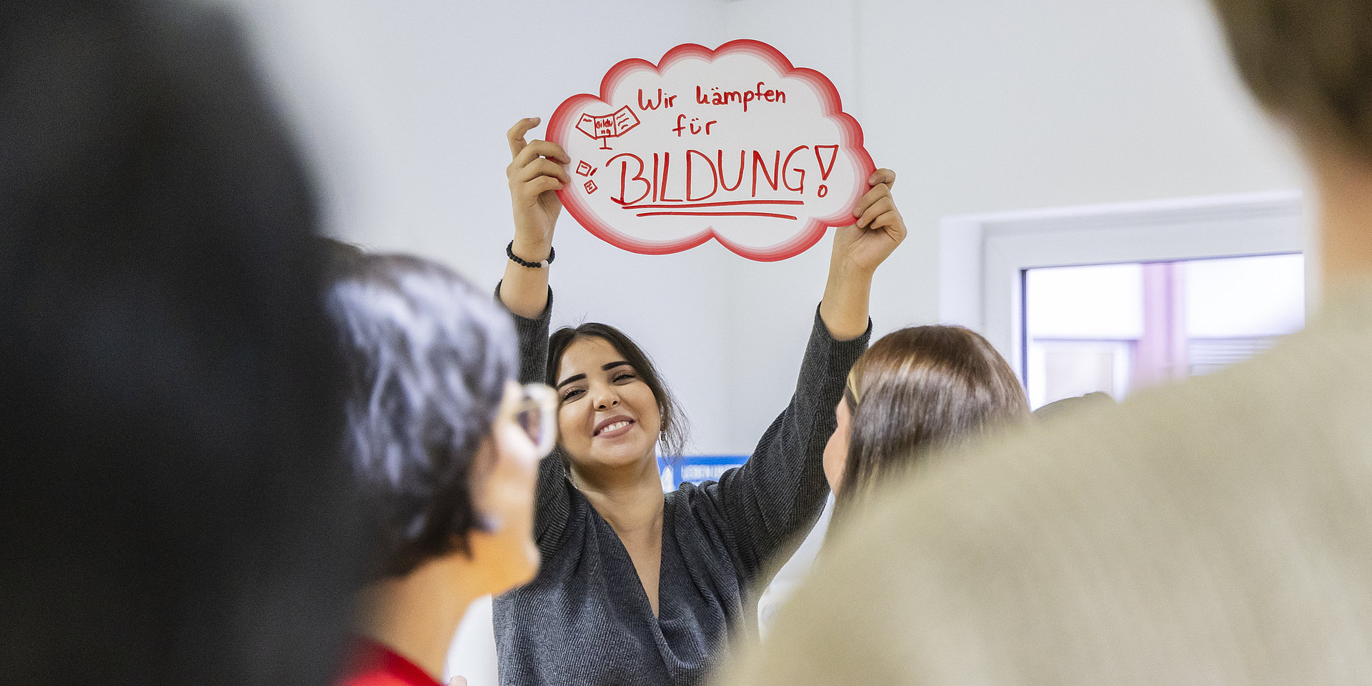Studentin hält während des Workshops ein rot umrandetes Schuld mit den Worten „Wir kämpfen für Bildung“ hoch. 