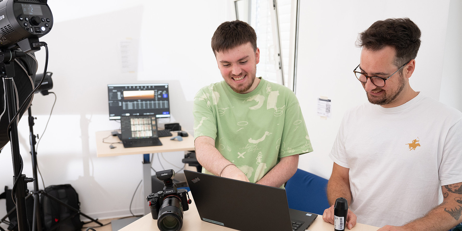 Two computer science students are standing side by side at a computer.