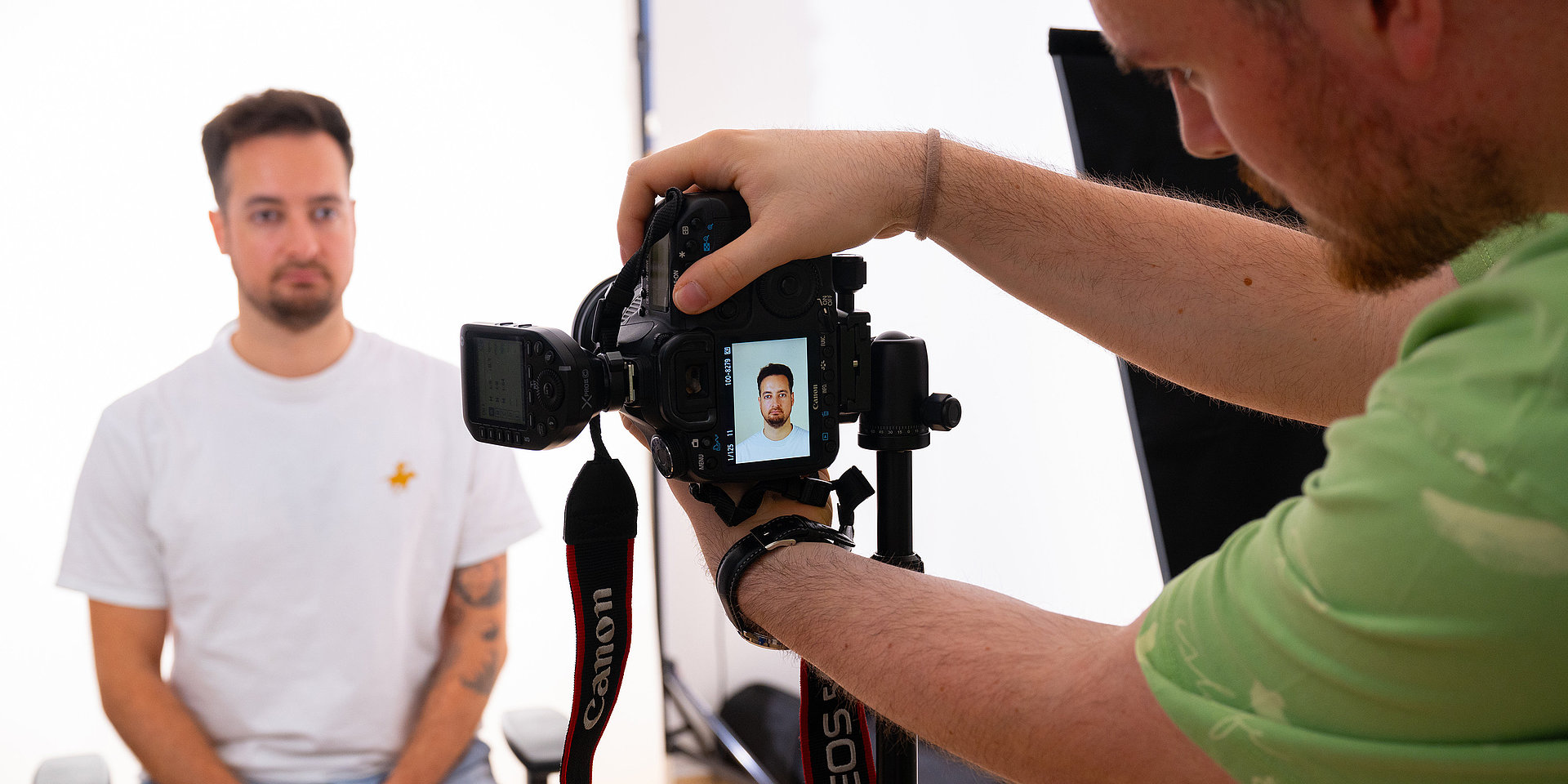 Person sitzt vor weißem Hintergrund und wird im Studio frontal für Passfoto aufgenommen.