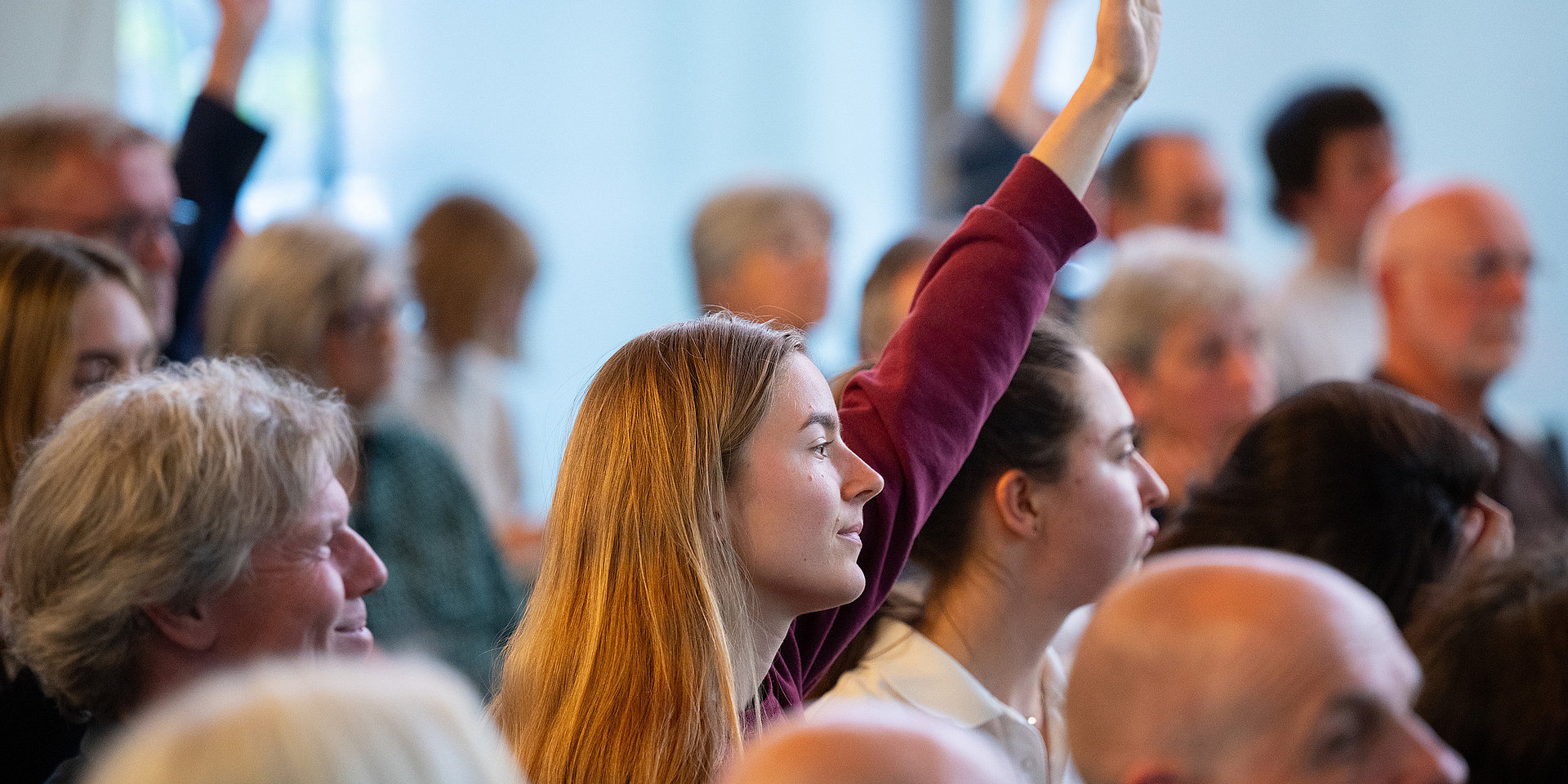 Several guests raise their hands to ask a question.