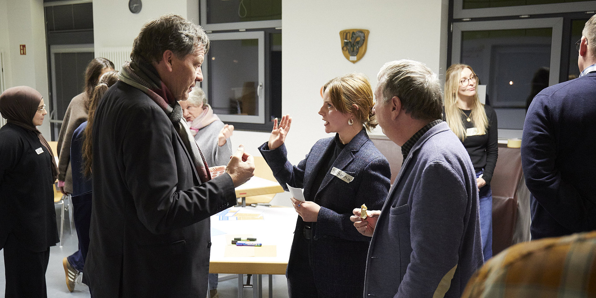 Studentin in Diskussion mit zwei Besuchern.